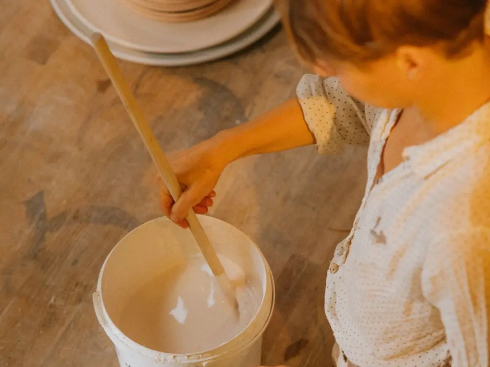 A potter stirring a bucket of glaze in the studio