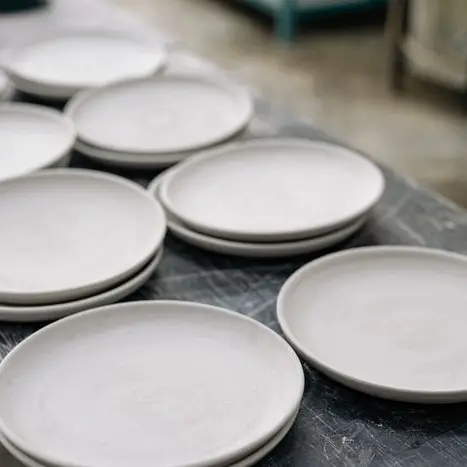 Stacks of matte white handmade clay plates on a studio table
